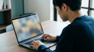 ノートパソコンの前で操作しながら考える男性の後ろ姿